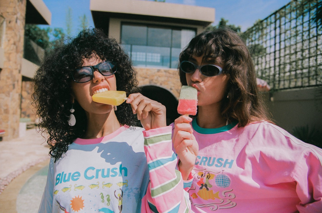 Two friends in Spicy Dugong striped tees eating ice blocks poolside
